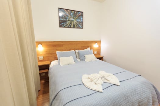 Chambre confortable avec lit double, linge de lit bleu et décoration murale moderne. Éclairage doux et ambiance accueillante.