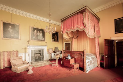 Chambre du Château de Sainte-Julie avec lit à baldaquin, cheminée, fauteuils et tableaux accrochés aux murs.