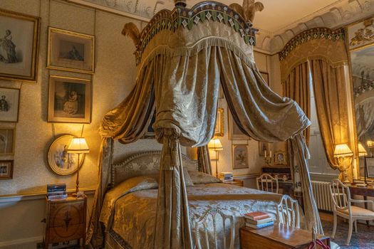 Chambre élégante du Château de Sainte-Julie avec un lit à baldaquin, des tableaux et des lampes douces.