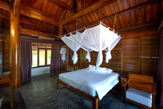 Chambre spacieuse avec lit à baldaquin, décor en bois et grandes fenêtres offrant une vue sur l'extérieur.